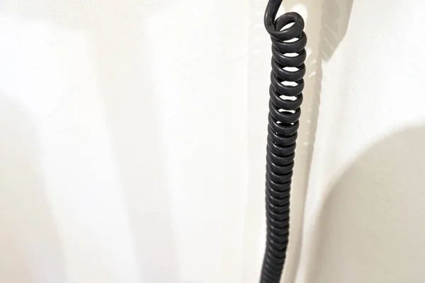 Spiralförmiges schwarzes Federtelefonkabel an weißer Wand — Stockfoto