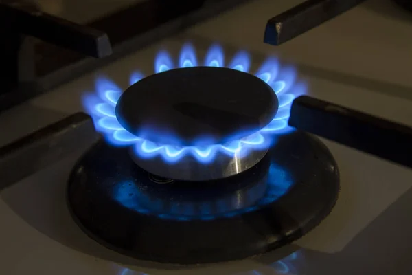 Burning gas stove hob blue flames close up in the dark on a blac — Stock Photo, Image