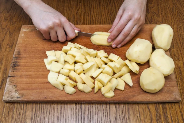 Женская рука с ножом, режущим картошку на деревянном боа — стоковое фото