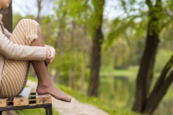 Füße der schönen jungen Frau sitzen auf Bank im Park. — Stockfoto