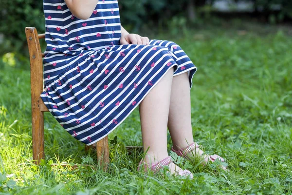 Ben och fötter av liten flicka i klänning som sitter på en stol på gree — Stockfoto