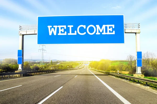 Blue freeway sign over the road on sunny day with word Welcome o — Stock Photo, Image