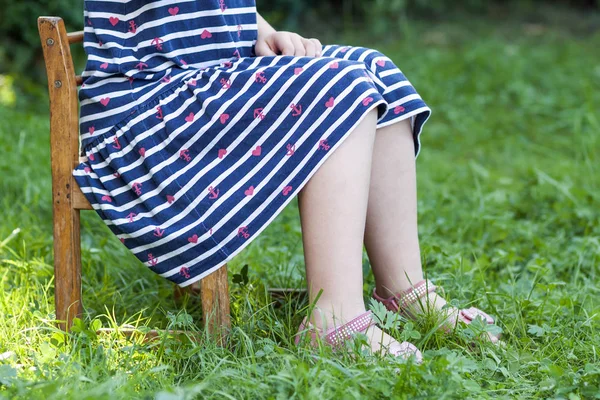Las piernas y los pies de la niña en vestido sentado en una silla en Gree — Foto de Stock