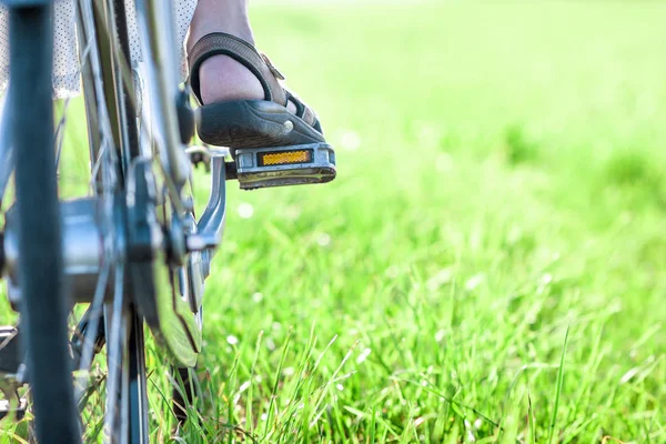 Womans foot on bicycle pedal on green grass closeup