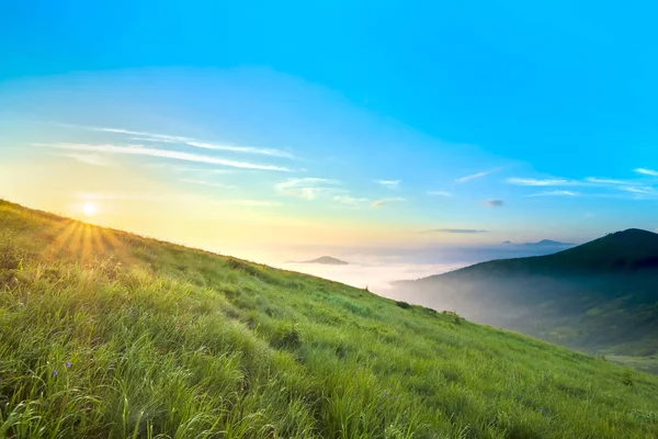 Salida del sol sobre colinas en montañas con hierba verde y cielo azul wi — Foto de Stock