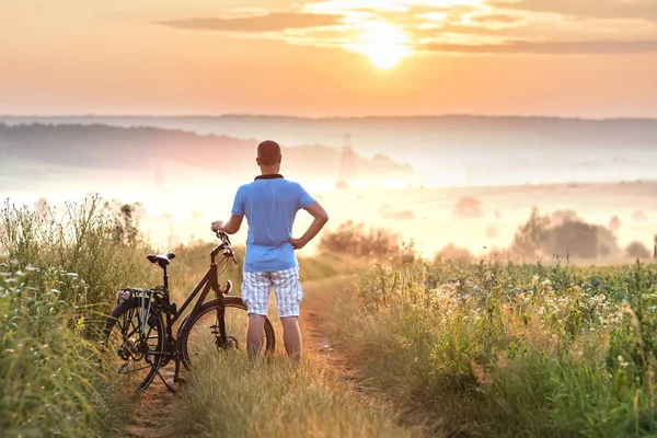 Young man standing near  bicycle in morning sunrise with wonderf