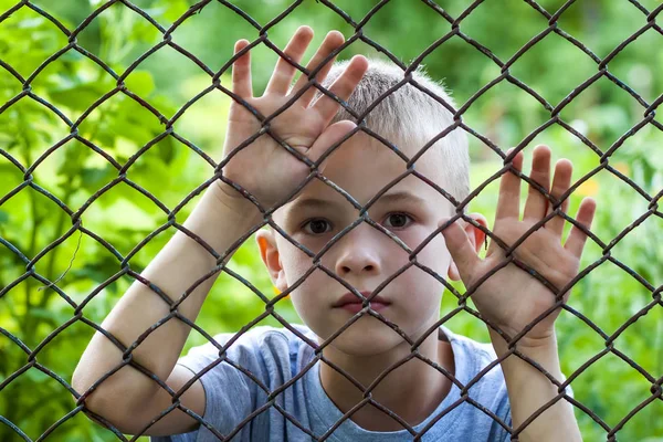 Retrato de un niño detrás de una cerca de eslabones de cadena — Foto de Stock