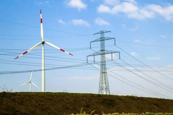 High voltage tower and wind turbines against blue sky