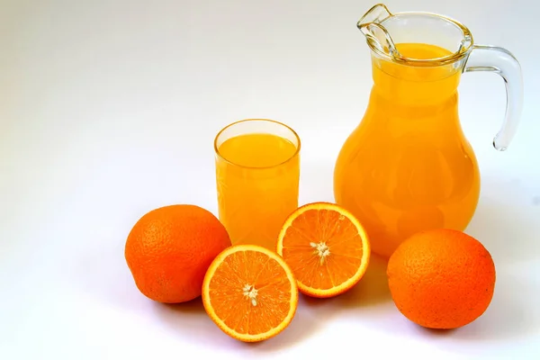 Dzbanek i szklankę soku pomarańczowego i dojrzałych pomarańczy na białym tle — Zdjęcie stockowe