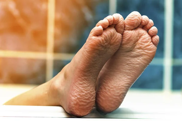 Wrinkled bare feet coming out from a bathtub. Young person getti