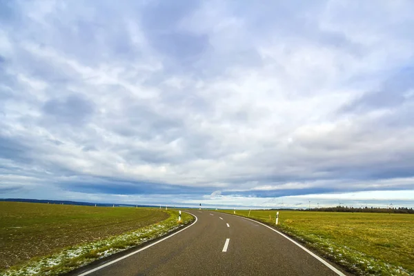 Пустая чёрная асфальтовая дорога между зелёными полями — стоковое фото