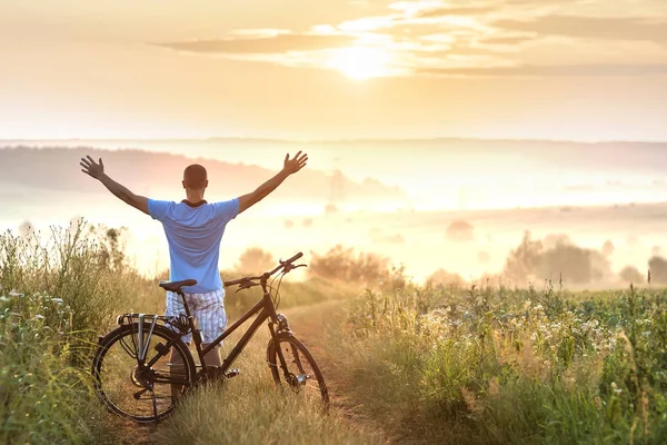 Young man standing near  bicycle in morning sunrise with wonderf