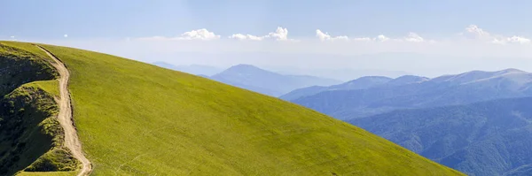 Панорама зеленых холмов в летних горах с гравийной дорогой для — стоковое фото