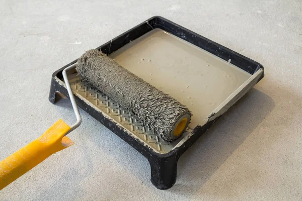 Paint roller in paint tray with grey color in the tray