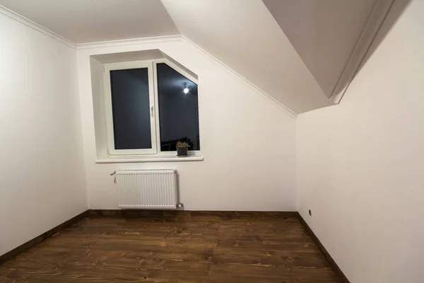 Piccola stanza vuota con pavimento in parquet di legno di quercia, pareti bianche dipinte di recente, radiatore di riscaldamento e una finestra. Camera mansardata — Foto Stock