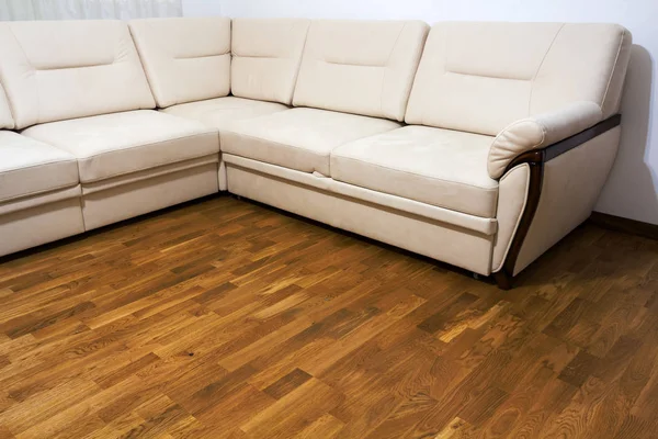 Большой бежевый диван на деревянном паркетном полу — стоковое фото