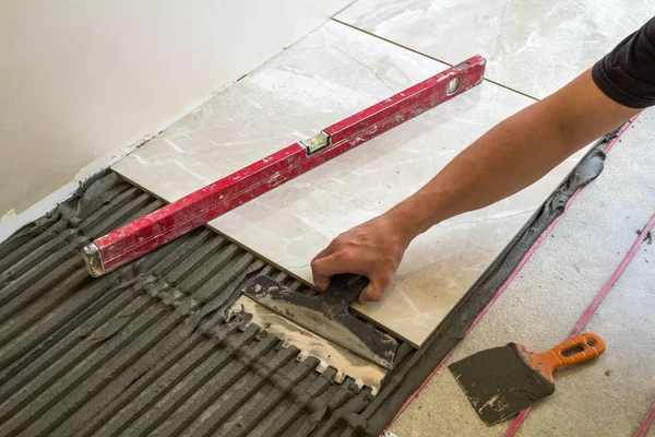 Keramische tegels en hulpmiddelen voor de tegelzetter. Werknemer hand vloertegels installeren. Verbetering van het huis, renovatie - keramische tegel vloer lijm, mortel, niveau. — Stockfoto