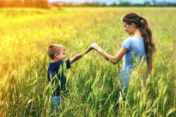 Mujer joven y niño pequeño su hijo de pie en el campo de trigo. Uni — Foto de Stock