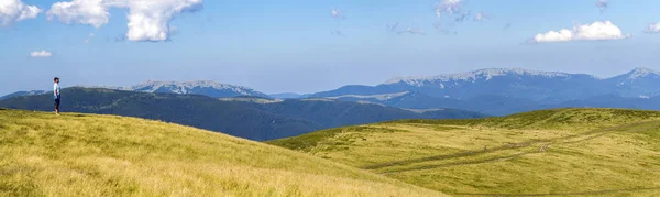 Одинокий турист, стоящий на широком холме с видом на горы — стоковое фото