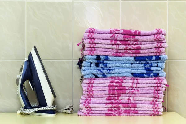 Ironing linen with steam generator. A stack of ironed towels lyi