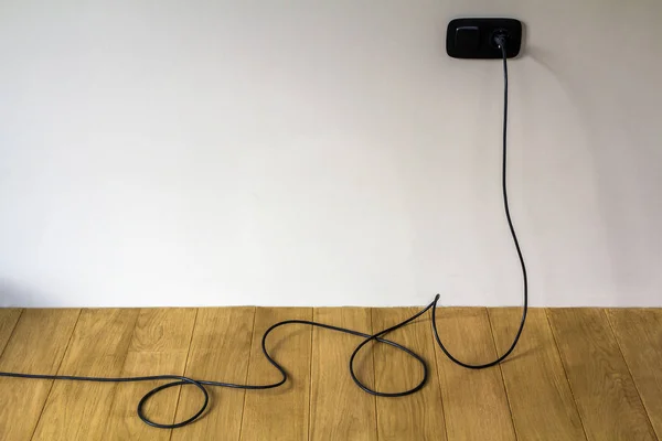 Cable eléctrico negro en zócalo de pared en suelo de parquet de madera —  Fotos de Stock