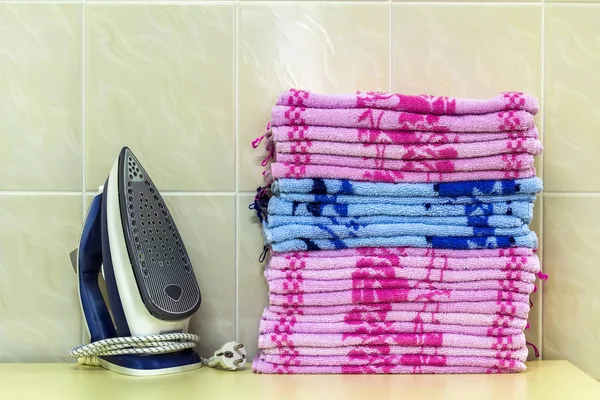 Ironing linen with steam generator. A stack of ironed towels lyi