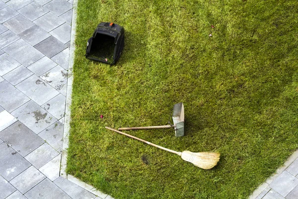 Jug dustpan and a broom on a green grass lawn. Gardening tools. — Stock Photo, Image