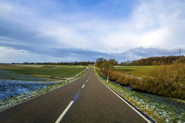 Пустая чёрная асфальтовая дорога между зелёными полями — стоковое фото