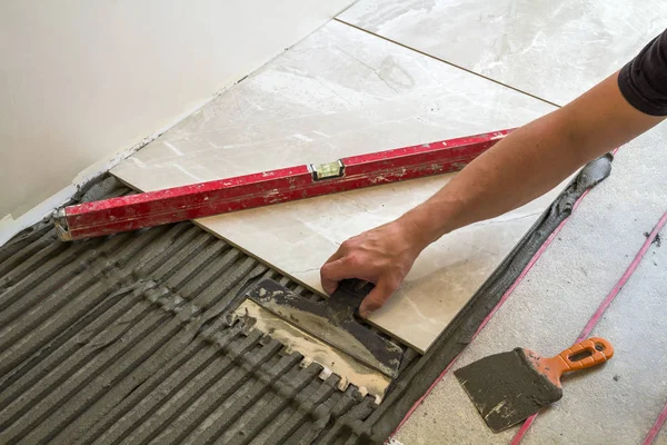 Keramische tegels en hulpmiddelen voor de tegelzetter. Werknemer hand vloertegels installeren. Verbetering van het huis, renovatie - keramische tegel vloer lijm, mortel, niveau. — Stockfoto