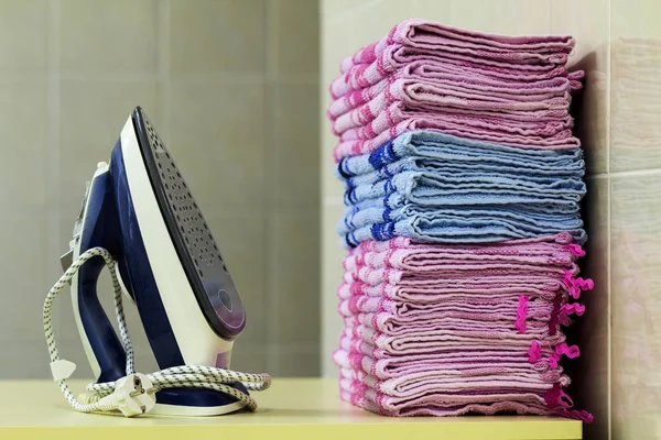 Ironing linen with steam generator. A stack of ironed towels lyi
