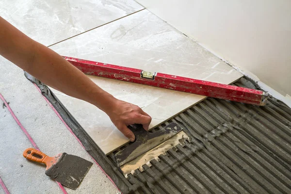 Ceramic tiles and tools for tiler. Worker hand installing floor tiles. Home improvement, renovation - ceramic tile floor adhesive, mortar, level. — Stock Photo, Image