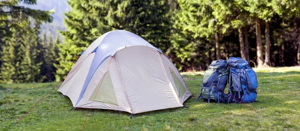 Campamento turístico en pradera verde con césped fresco en el bosque de las montañas de los Cárpatos. Caminantes tienda y mochilas en el camping. Estilo de vida activo, actividad al aire libre, vacaciones, deportes y concepto de recreación . —  Fotos de Stock