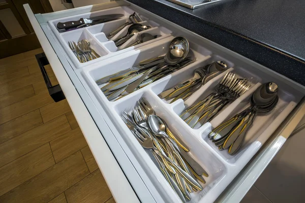 Ложки з нержавіючої сталі, виделки та ножі у ящику для столових приборів у білій кухонній шафі — стокове фото