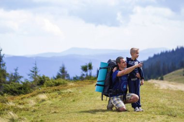 Baba ve oğul birlikte doğal hiking sırt çantaları ile yeşil dağlar yaz. Baba ve çocuk ayakta zevk dağ manzaralı manzara. Aktif yaşam tarzı, aile ilişkileri, hafta sonu etkinlik kavramı.
