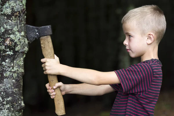 Kleine jongen met zware oude IJzeren bijl snijden boom troef in bos op zomerdag. Outdoor activiteiten en fysieke arbeid. — Stockfoto