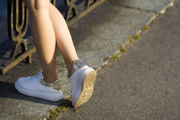 Zbliżenie na piękne szczupłe nogi młoda dziewczyna w białe trampki stojąc na beton markowania pokryć w starych żelazne ogrodzenie czeka na kogoś lub coś. Młodzieży, zdrowia i urody. — Zdjęcie stockowe