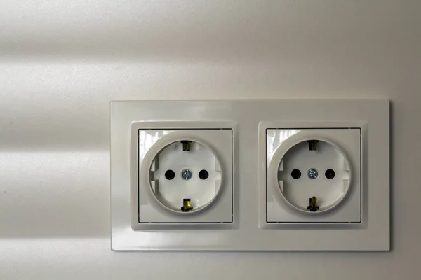 Nieuwe witte glanzende kunststof elektrische dubbele sockets op witte muur achtergrond. Voordelen en comfort van moderne huizen. — Stockfoto