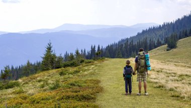 Baba ve oğul birlikte doğal hiking sırt çantaları ile yeşil dağlar yaz. Baba ve çocuk ayakta zevk dağ manzaralı manzara. Aktif yaşam tarzı, aile ilişkileri, hafta sonu etkinlik kavramı.