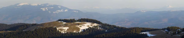 春先にぼやけている強大な遠い山脈の背景に乾いた草と雪のスポットの壮大なカルパティア山の谷の景色 — ストック写真