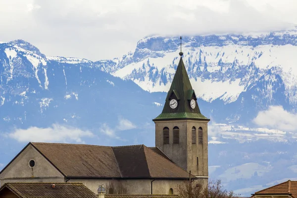 Dunkle Kontrastsilhouette von Kirchendach mit Turm vor herrlichen Alpenbergen, Deutschland. ruhiges Leben auf fantastischen Gipfeln mit glänzendem Schnee unter strahlend blauem Himmel mit geschwollenen weißen Wolken Hintergrund. — Stockfoto