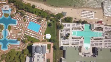 Okyanus kıyısındaki otellerin yukarıdan görünüşü mavi sulu yüzme havuzları ve sarı kumlu plajlar..