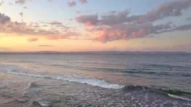 Gün batımında gökyüzünün altında mavi su dalgaları olan bir deniz yüzeyinin havadan görünüşü.