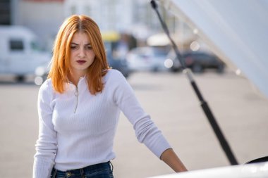 Stresli genç bir kadın sürücü kırık bir arabanın yanında duruyor.