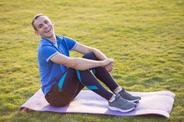 Genç sporcu adam antrenman minderinde oturuyor.