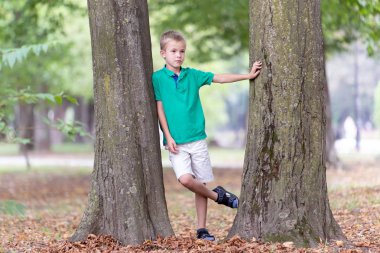 Büyük bir ağaç gövdesinin yanında duran sevimli bir çocuğun portresi.