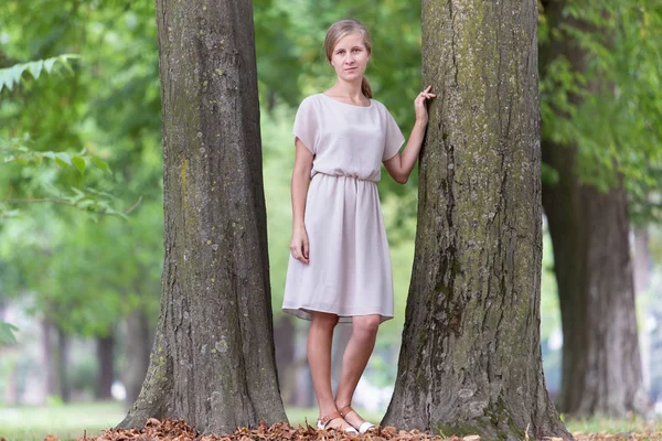 Retrato de una joven mujer de pie cerca de un gran tronco de árbol en verano — Foto de Stock