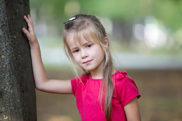 Retrato de una niña bonita de pie cerca del árbol grande tr —  Fotos de Stock