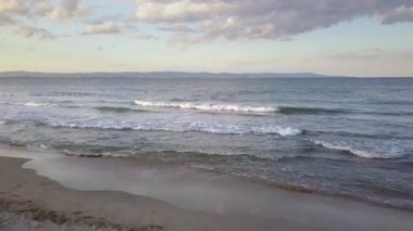 Gün batımında gökyüzünün altında mavi su dalgaları olan bir deniz yüzeyinin havadan görünüşü.