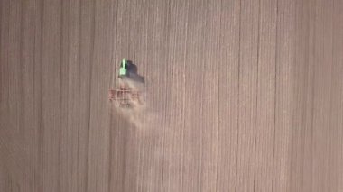 Yeşil traktörün havadan görünüşü, toprağı işlemesi ve kuru bir tarlayı tohumlaması. Çiftçi, bahar başlarında tohum ekme faaliyetlerinin bir parçası olarak tohum ekicisiyle arazi hazırlıyor.