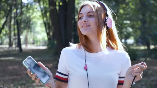 漂亮的少女红头发听音乐在户外的夏季公园 — 图库视频影像